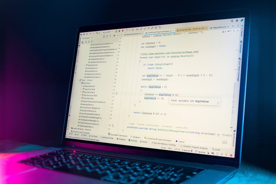 A close-up view of a laptop screen displaying lines of programming code in a text editor, with a dark background and a pink and blue glow emanating from the keyboard area. The code appears to be writt